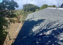 Newly installed gray asphalt shingles on pitched residential roof with tree shadows