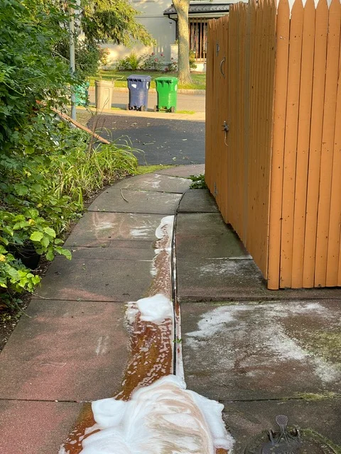 White gutter and downspout system installed along wooden fence with proper water drainage