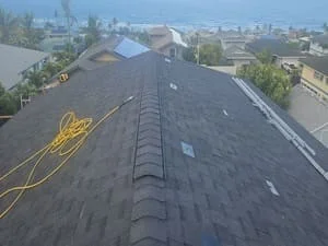 Newly installed dark asphalt shingle roof with ridge cap and ventilation components