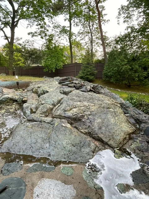 Large granite boulders arranged in landscape with water feature and mature trees