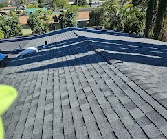 Gray asphalt shingles installed on residential roof with blue membrane flat roof section