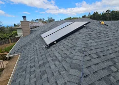 Gray asphalt shingle roof with solar panel array and brick chimney