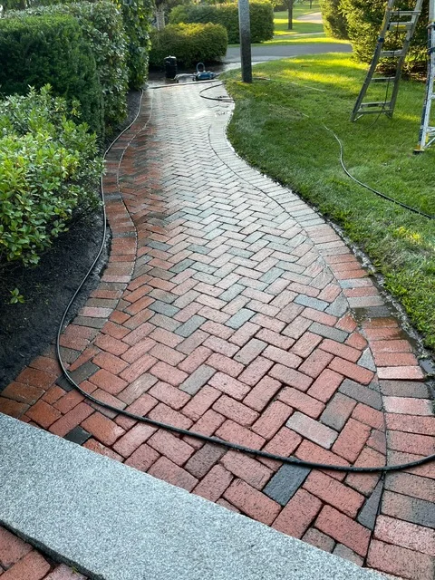 Red and charcoal brick pavers in herringbone pattern forming curved walkway with landscape edging