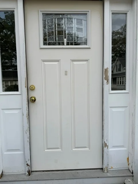 White entry door with transom window and sidelights, brass hardware, raised panel construction