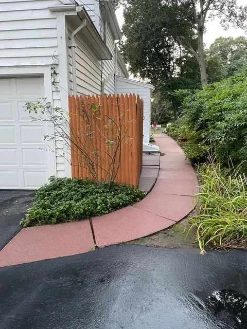 Red concrete driveway with curved edging, wooden fence, and landscape plantings along home exterior