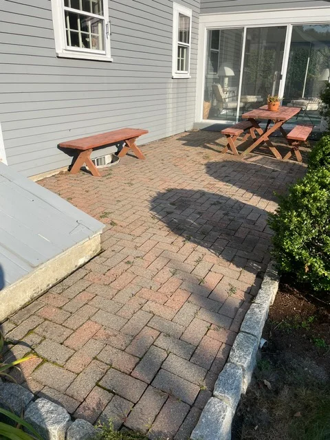 Brick and charcoal paver patio with wooden picnic tables and concrete edging