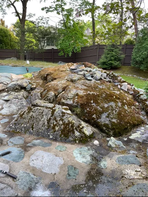 Large moss-covered boulders with stone base installation in residential landscape