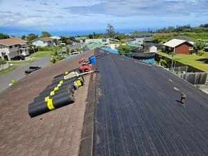 Aerial view of residential roof with new asphalt shingles being installed, staged materials and equipment visible