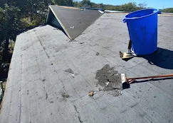 Flat roof with gray asphalt membrane showing wear, damage assessment in progress