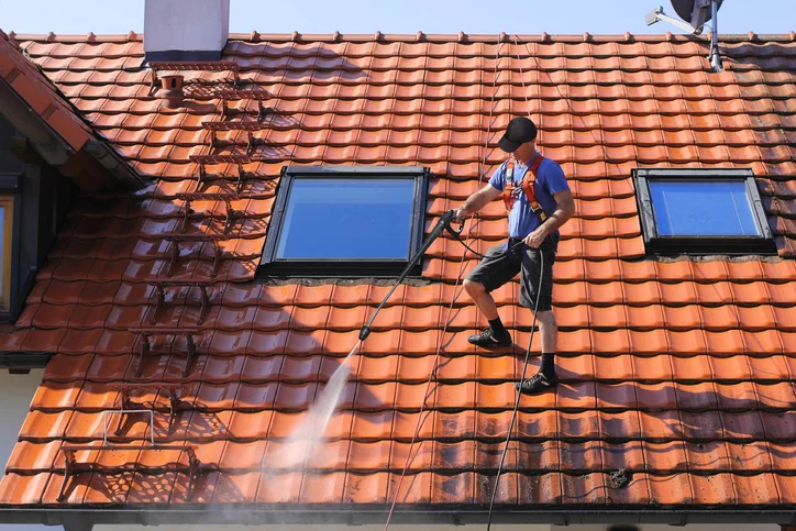Worker pressure washing clay tile roof with skylights using safety harness