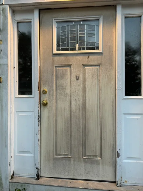 Two-panel wood entry door with grid window and sidelights, brass hardware, stucco surround