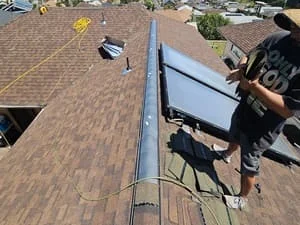 Asphalt shingle roof installation with brown dimensional shingles and metal ridge flashing