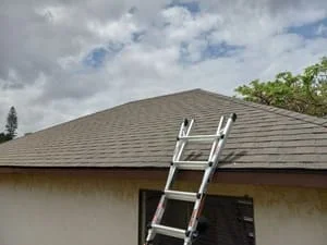 Hip roof with gray asphalt shingles during installation with ladder access