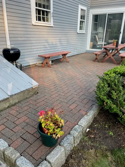 Brick paver patio with herringbone pattern, concrete edging, and wooden benches against blue siding home