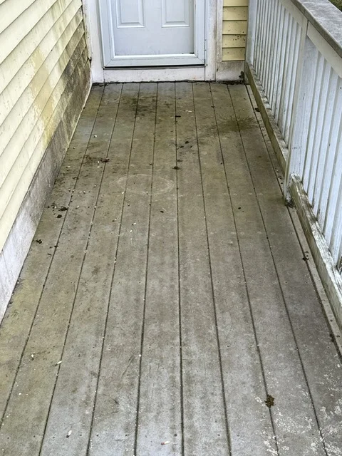 Wooden deck boards cleaned and prepared, flanked by white vinyl siding and railing