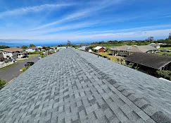 Gray asphalt shingles installed on residential roof with clear sky and neighborhood in background
